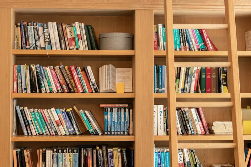 Rayonnages en bois blond chargés de livres, avec une échelle en bois appuyée contre les étagères.