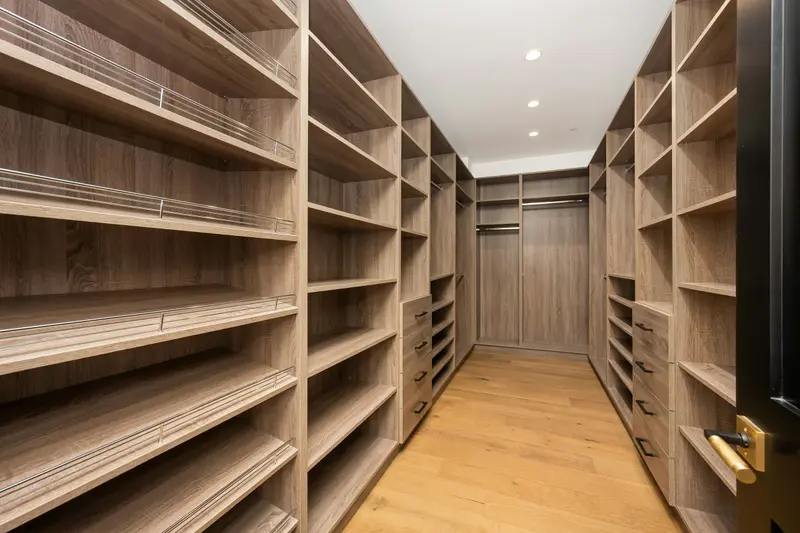 Dressing vide en forme de couloir, bordé de part et d'autre d'étagères en bois clair du sol au plafond, éclairé par des spots.
