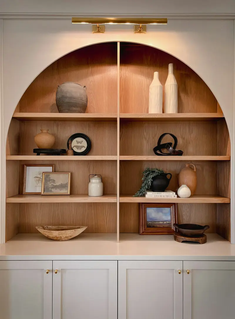 Étagères en bois clair dans une niche en arc, garnies de poteries, de cadres et d'objets de décoration.